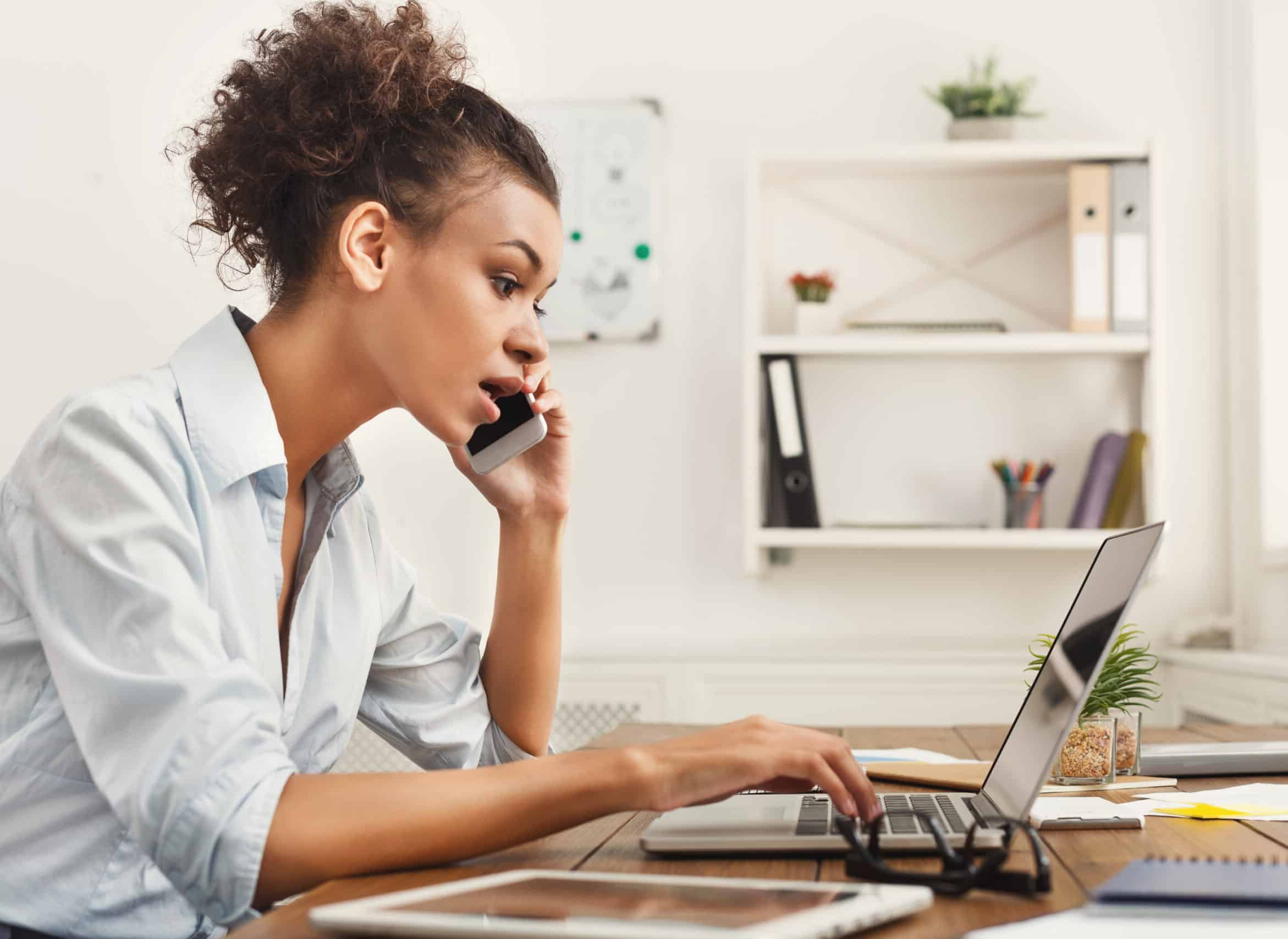 Concentrated african-american business woman at work talking on phone, sitting at her working place in office, copy space