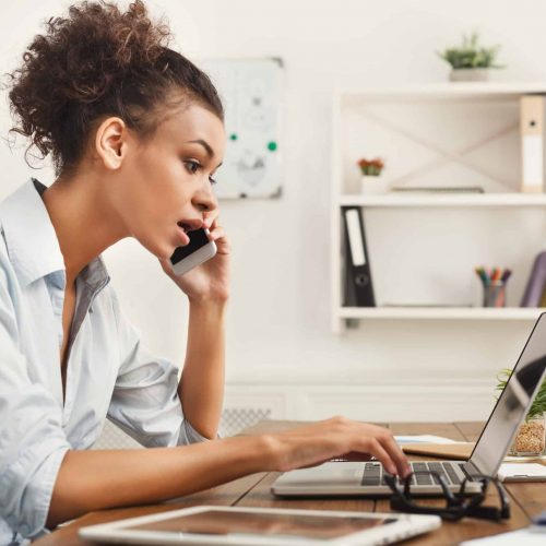 Concentrated business woman talking on phone Concentrated african-american business woman at work talking on phone, sitting at her working place in office, copy space