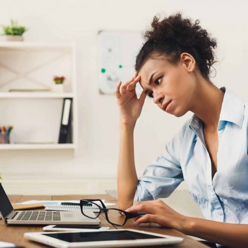 Frustrated business woman with headache at office Deadline stress concept - sad african-american business woman sitting at desktop in office, working on laptop and holding hand on head. Hard working day, copy space